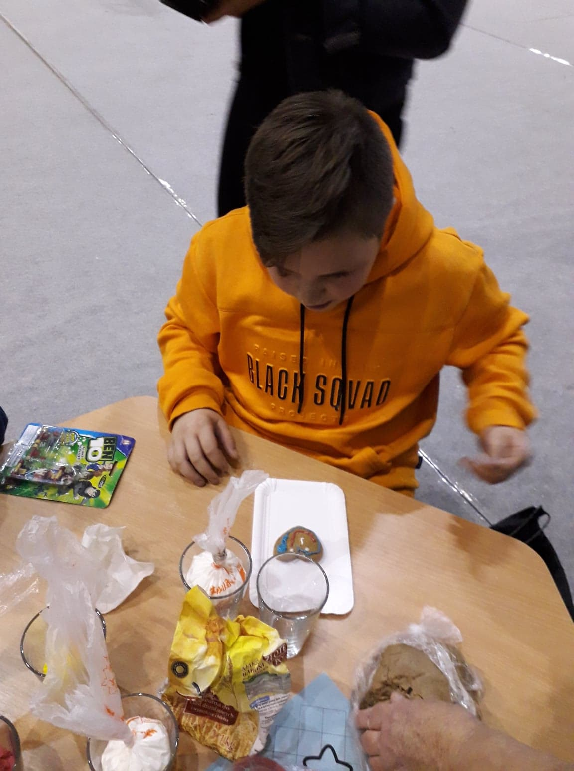 Cłopiec siedzący przy stole, zdobiący lukrem pierniczek.