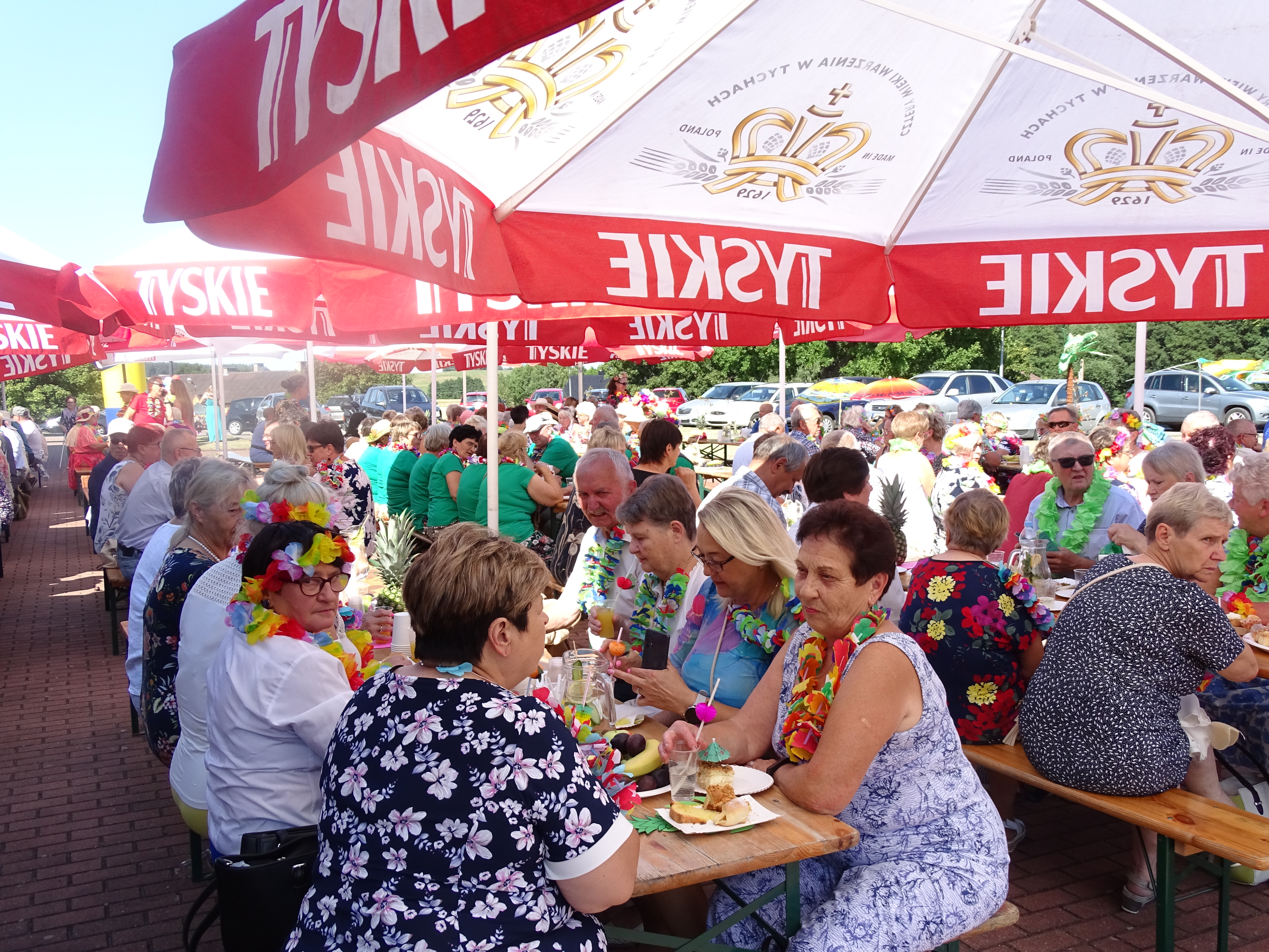 Uczestnicy pikniku zgromadzeni przy stołach pod parasolami